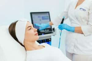 cosmetologia clinica. professionale femmina cosmetologo fare idrofacciale procedura mentre essere un' opera. attraente simpatico donna dire bugie su il medico letto mentre avendo bellezza procedure foto