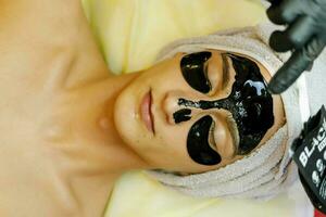 il cosmetologo mette un' maschera su il viso di un' giovane uomo. foto