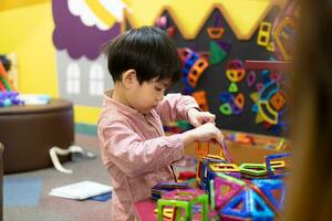 un' poco asiatico ragazzo è giocando con un' piazza magnetico puzzle. foto