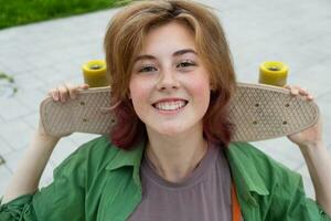 femmina skateboarder ritratto. adolescenziale pattinatore ragazza sorridente Tenere skateboard. foto