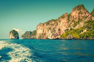 scogliera e il chiaro mare con un' barca vicino phi phi isola nel Sud di Tailandia foto