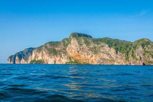 scogliera e il chiaro mare con un' barca vicino phi phi isola nel Sud di Tailandia foto