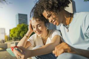 afro americano e caucasico coppia guardare il Telefono, ascoltando per musica e ridendo nel il città. foto
