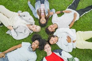 gruppo di multietnico amici posa giù nel un' cerchio su il erba nel il parco foto