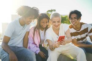 gruppo di contento adolescenziale amici guardare il Telefono e ridendo nel il città strada con sole leggero foto