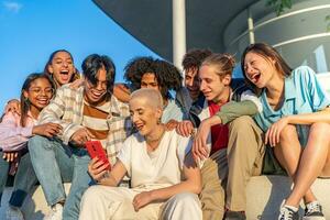 gruppo di contento adolescenziale amici ridendo e guardare il Telefono nel il strada durante d'oro ora foto