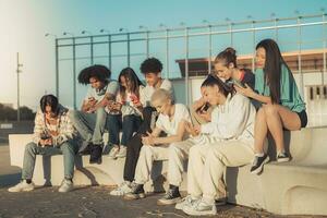 grande gruppo di contento adolescenziale amici ogni uno guardare a loro Telefono nel un' panchina nel il strada. foto