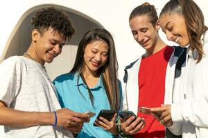 gruppo di contento adolescenziale amici guardare loro telefoni e ridendo nel il città strada. foto