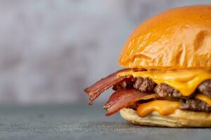 vicino su di gustoso hamburger al formaggio con Bacon su grigio sfondo. foto