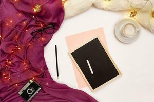 un' tazza di caffè, un' piccolo nero di legno tavola e un' bianca gesso con nuovo anni obiettivi. sciarpa e Natale luci su bianca sfondo. foto