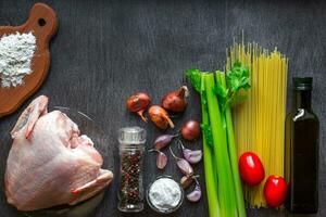 pasta ingredienti. pollo seni, ciliegia pomodori, spaghetti pasta, elery, spezie e aglio su il di legno tavolo. spazio per testo. foto