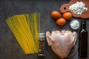 cucinato spaghetti tagliatelle. crudo spaghetti e crudo pollo su tavola. ingredienti per fatti in casa tagliatelle pollo uova, verdura olio. il buio nero legna sfondo. superiore Visualizza. foto