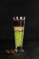 ghiacciato avocado caffè, fresco miscelato avocado versato uno tiro di caffè espresso nel un' plastica tazza su un' di legno sottobicchiere foto