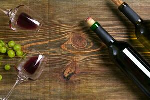 rosso e bianca vino bottiglie, uva e bicchieri al di sopra di di legno tavolo. superiore Visualizza con copia spazio foto