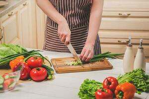 giovane donna cucinando nel il cucina a casa. un' donna tagli un' verde cipolla e verdure con un' coltello. foto