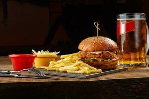 gustoso hamburger, francese patatine fritte con salsa e bicchiere di birra su nero tavola foto