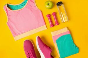 fitness Accessori su giallo sfondo. scarpe da ginnastica, bottiglia di acqua, manubri e sport superiore. foto