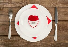 San Valentino giorno cena tavolo ambientazione con rosso scatola, squillo, coltello e forchetta al di sopra di quercia sfondo. foto