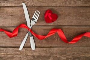 San Valentino giorno cena tavolo ambientazione con rosso nastro, coltello e forchetta squillare al di sopra di quercia sfondo. foto