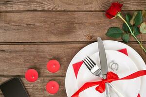 San Valentino giorno cena tavolo ambientazione con rosso nastro, rosa, coltello e forchetta squillare al di sopra di quercia sfondo. foto