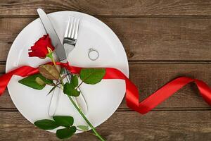 san valentino giorno tavolo ambientazione con piatto, forchetta, coltello, squillo, nastro e rosa. sfondo foto