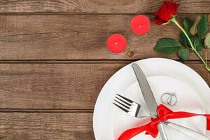 San Valentino giorno cena tavolo ambientazione con rosso nastro, rosa, coltello e forchetta squillare al di sopra di quercia sfondo. foto