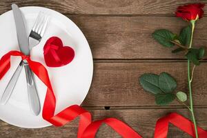 san valentino giorno tavolo ambientazione con piatto, forchetta, coltello, rosso cuore, nastro e rosa. sfondo foto