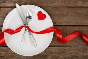 san valentino giorno tavolo ambientazione con piatto, forchetta, coltello, rosso cuore e nastro. sfondo foto