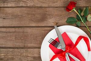 san valentino giorno tavolo ambientazione con piatto, forchetta, coltello, nastro e rosa. sfondo foto