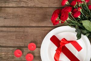 superiore Visualizza avvicinamento di romantico cena servendo con un' mazzo rosso Rose e presente sopra il bianca piatto foto