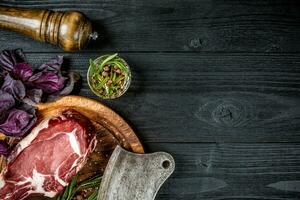 fresco crudo Manzo con basilico e un' rametto di rosmarino con ascia per carne su nero di legno sfondo. superiore Visualizza foto