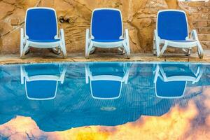 sedie a sdraio vicino nuoto piscina e riflessa loro nel blu acqua foto