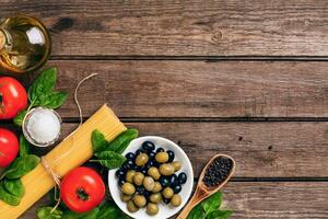 crudo ingredienti per il preparazione di italiano pasta, spaghetti, basilico, pomodori, olive e oliva olio su di legno sfondo. superiore Visualizza. copia spazio. foto