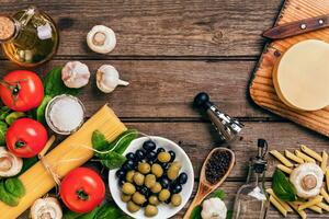 crudo ingredienti per il preparazione di italiano pasta, spaghetti, basilico, pomodori, olive e oliva olio su di legno sfondo. superiore Visualizza. copia spazio. foto