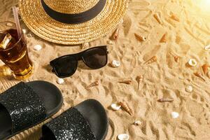 estate abbigliamento da spiaggia, Flip flop, cappello, freddo bevanda nel un' bicchiere e conchiglie su sabbia spiaggia. foto