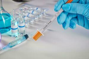 mani nel blu guanti Tenere analisi kit. medico fiaschi con colorato chimico reagenti. fiale e siringa isolato su bianca. coronavirus foto