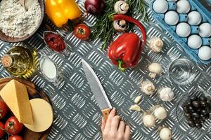 femmina mano con coltello su metallo cucina tavolo, in giro menzogna ingredienti, la verdura, e spezie per Pizza. foto