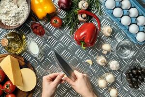femmina mano con coltello su metallo cucina tavolo, in giro menzogna ingredienti, la verdura, e spezie per Pizza. foto