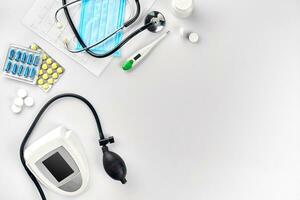 bianca elettrico tonometro con stetoscopio, multicolore pillole, maschera e termometro su bianca tavolo. superiore Visualizza foto