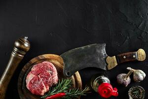 pezzo di Manzo filetto, con ascia per taglio e chopping carne, spezie erano cucinando - rosmarino, Pepe, sale, aglio. su vecchio di legno tavola su pietra nero tavolo. foto