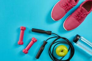 piatto posare di femmina sport attrezzature, saltare corda, bottiglia di acqua e rosa scarpe da ginnastica su blu sfondo foto