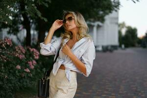 bellissimo biondo donna nel elegante moda casuale attrezzatura in posa su il strada. caldo tramonto colore. foto