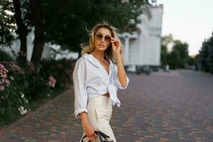 bellissimo biondo donna nel elegante moda casuale attrezzatura in posa su il strada. caldo tramonto colore. foto