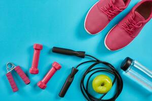 piatto posare di femmina sport attrezzature, saltare corda, bottiglia di acqua e rosa scarpe da ginnastica su blu sfondo foto