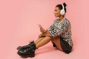 estatico donna con per favore ascoltando bello musica su rosa sfondo. Tenere mobile Telefono. indossare elegante camicetta e pelle gonna. foto