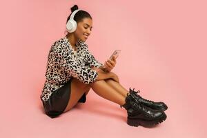 estatico donna con per favore ascoltando bello musica su rosa sfondo. Tenere mobile Telefono. indossare elegante camicetta e pelle gonna. foto