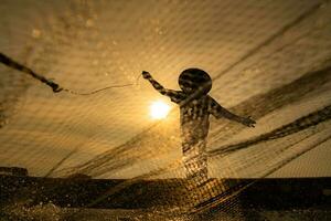 silhouette di pescatore a Alba, in piedi a bordo un' canottaggio barca e getto un' netto per catturare pesce per cibo foto