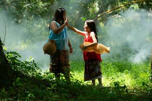Due ragazze asiatico donne con tradizionale capi di abbigliamento In piedi nel il foresta pluviale. essi aveva divertimento giocando insieme prima assistere Nonno nel attraente pesce nel un' nelle vicinanze lago. foto