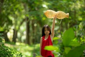 poco asiatico ragazza nel rosso vestito Tenere pesca attrezzatura nel il foresta, rurale Tailandia vivente vita concetto foto