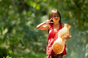 poco asiatico ragazza nel rosso vestito Tenere pesca attrezzatura nel il foresta, rurale Tailandia vivente vita concetto foto